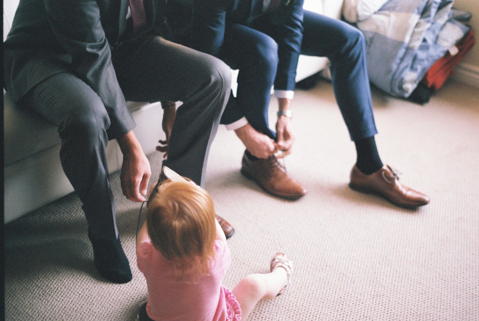 Baby sitting on floor while men in suits tie their shoelaces